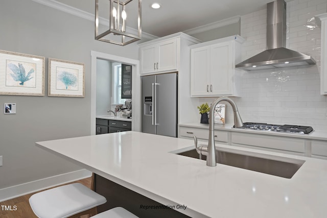 kitchen featuring wall chimney exhaust hood, white cabinetry, stainless steel appliances, and decorative light fixtures