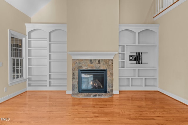 unfurnished living room featuring built in shelves, a stone fireplace, and light hardwood / wood-style flooring