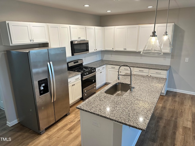 kitchen featuring appliances with stainless steel finishes, sink, pendant lighting, white cabinets, and hardwood / wood-style flooring