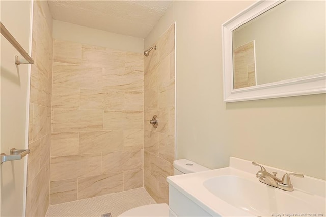 bathroom featuring toilet, a textured ceiling, vanity, and a tile shower