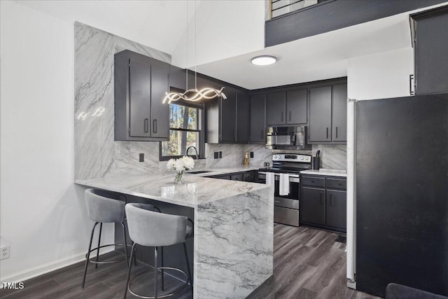 kitchen featuring dark wood-type flooring, kitchen peninsula, hanging light fixtures, sink, and appliances with stainless steel finishes