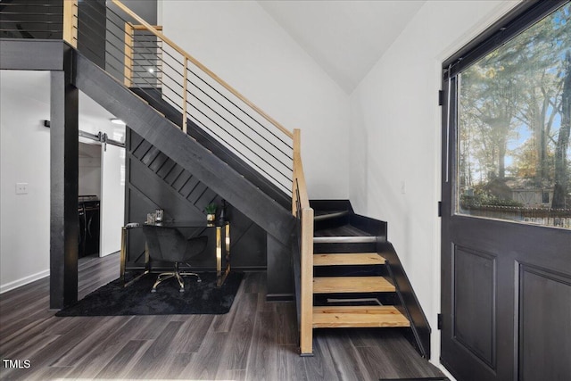 stairs with a barn door, hardwood / wood-style flooring, and vaulted ceiling