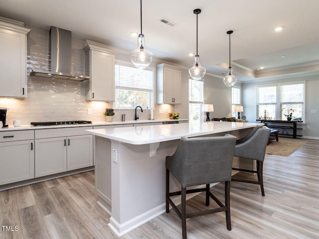 kitchen with wall chimney range hood, a kitchen island, gas stovetop, plenty of natural light, and light hardwood / wood-style floors