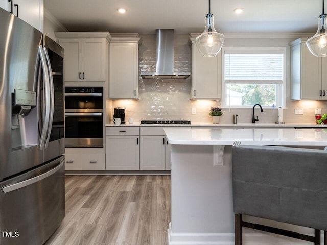 kitchen with wall chimney exhaust hood, pendant lighting, white cabinets, and stainless steel appliances