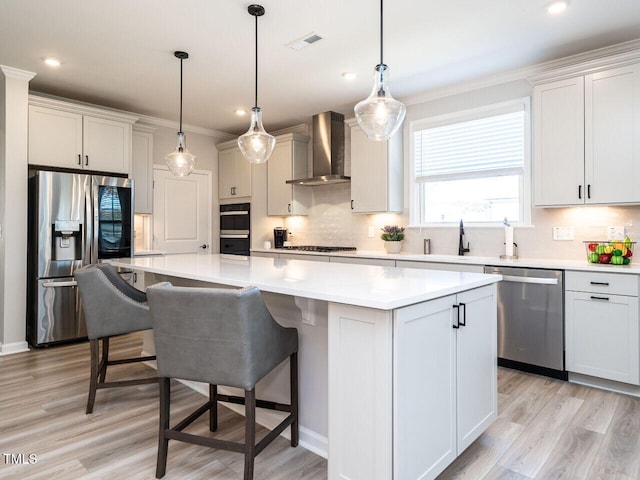 kitchen featuring hanging light fixtures, a center island, appliances with stainless steel finishes, and wall chimney range hood