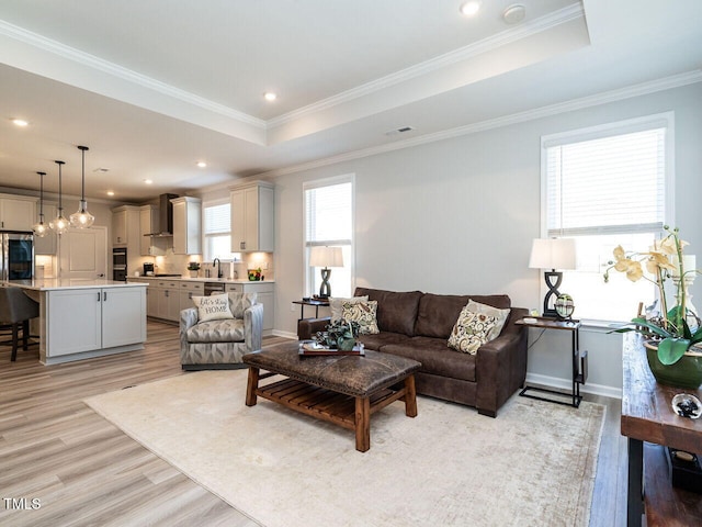 living room with sink, crown molding, a tray ceiling, and light wood-type flooring