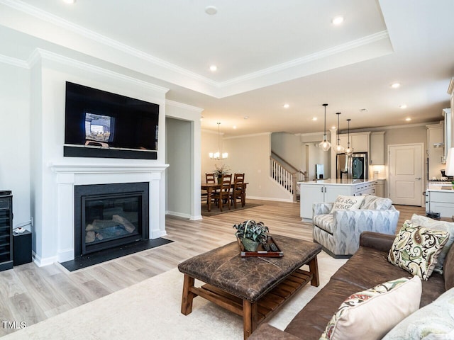 living room with light hardwood / wood-style flooring, ornamental molding, a notable chandelier, and a raised ceiling