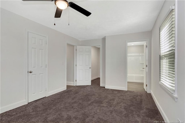 unfurnished bedroom with ceiling fan, ensuite bath, and dark carpet