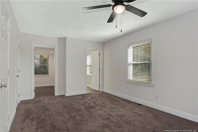 unfurnished bedroom with ceiling fan, dark carpet, multiple windows, and a textured ceiling