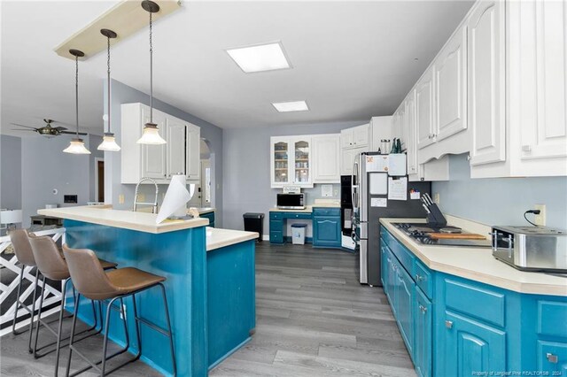 kitchen featuring light wood-type flooring, blue cabinets, decorative light fixtures, white cabinets, and black gas stovetop