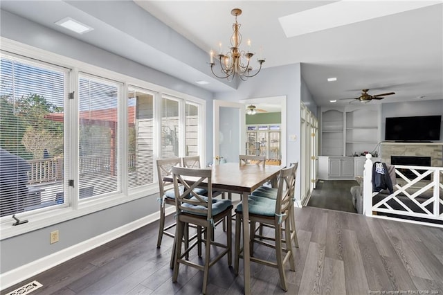 dining space featuring dark wood-type flooring, built in features, a skylight, and ceiling fan with notable chandelier