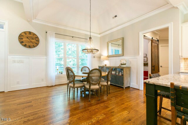 dining area with dark wood-type flooring, crown molding, a notable chandelier, and a barn door