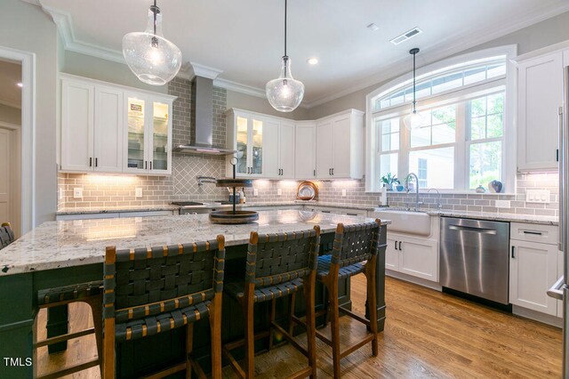 kitchen featuring a kitchen island, white cabinetry, stainless steel dishwasher, pendant lighting, and wall chimney exhaust hood