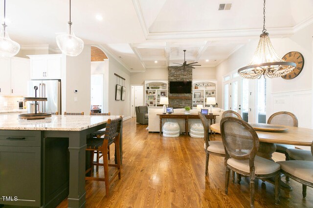 dining room with crown molding, light hardwood / wood-style flooring, a stone fireplace, and ceiling fan with notable chandelier