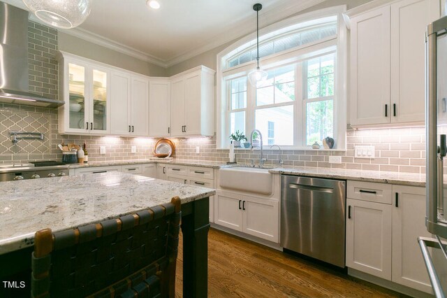 kitchen with sink, white cabinetry, stainless steel appliances, wall chimney exhaust hood, and pendant lighting