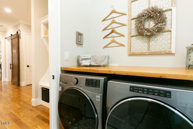 washroom with light hardwood / wood-style flooring, ornamental molding, a barn door, and washing machine and dryer