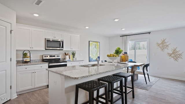 kitchen featuring appliances with stainless steel finishes, a kitchen breakfast bar, a kitchen island with sink, sink, and white cabinetry