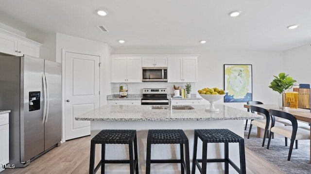 kitchen featuring white cabinets, stainless steel appliances, a kitchen island with sink, and light hardwood / wood-style flooring