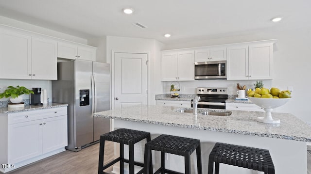 kitchen with white cabinets, stainless steel appliances, light hardwood / wood-style floors, and an island with sink