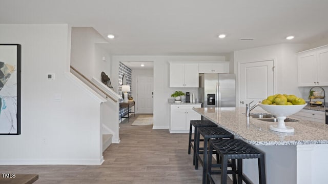 kitchen with light wood-type flooring, a kitchen island with sink, white cabinets, stainless steel fridge with ice dispenser, and a breakfast bar area