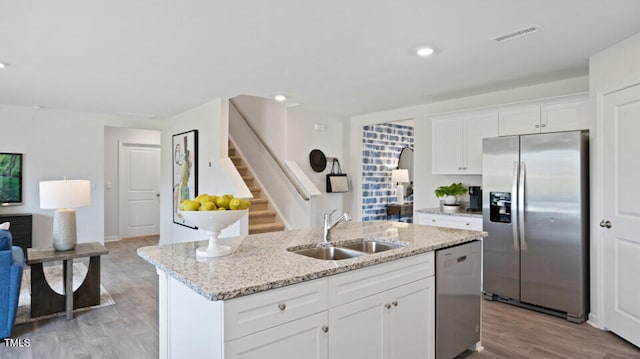 kitchen with white cabinets, sink, light wood-type flooring, an island with sink, and stainless steel appliances