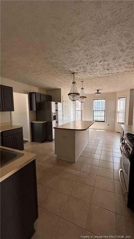 kitchen with a textured ceiling, electric stove, light tile patterned flooring, pendant lighting, and a center island