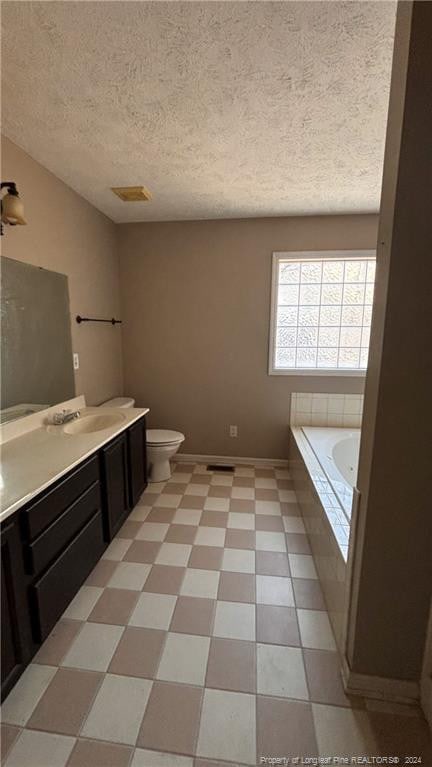 bathroom featuring vanity, a textured ceiling, tiled bath, and toilet