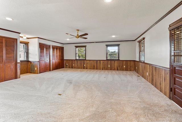 carpeted spare room featuring ornamental molding, wooden walls, a textured ceiling, and ceiling fan