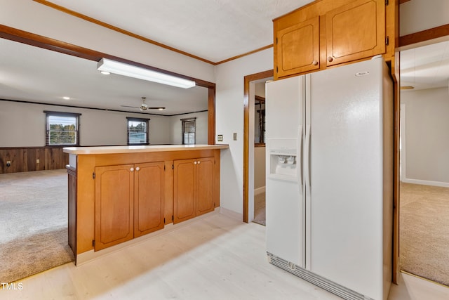 kitchen with kitchen peninsula, ceiling fan, white refrigerator with ice dispenser, crown molding, and wooden walls