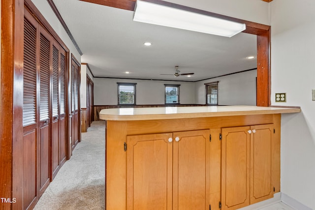 kitchen with kitchen peninsula, light colored carpet, ceiling fan, and crown molding