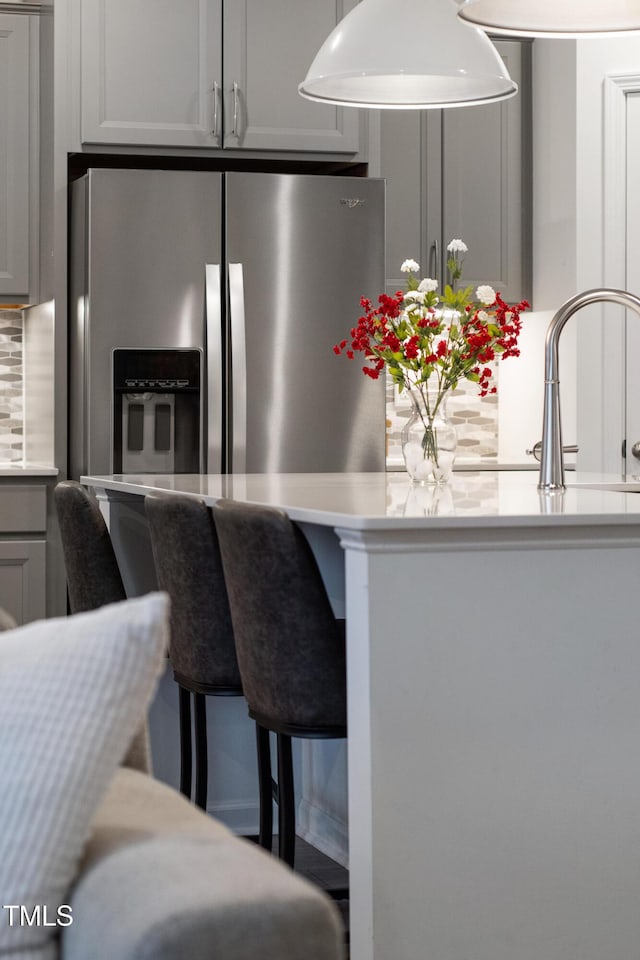 kitchen featuring stainless steel refrigerator with ice dispenser, light countertops, backsplash, a breakfast bar, and gray cabinetry