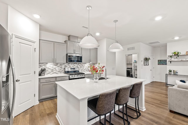 kitchen with stainless steel appliances, gray cabinets, a sink, a breakfast bar area, and backsplash