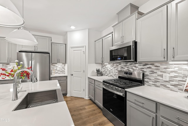 kitchen with stainless steel appliances, a sink, gray cabinetry, light countertops, and recessed lighting