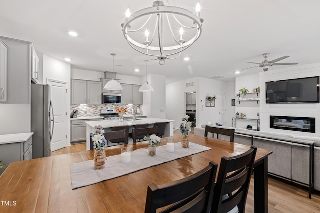dining area featuring ceiling fan, recessed lighting, light wood-type flooring, a chandelier, and a fireplace