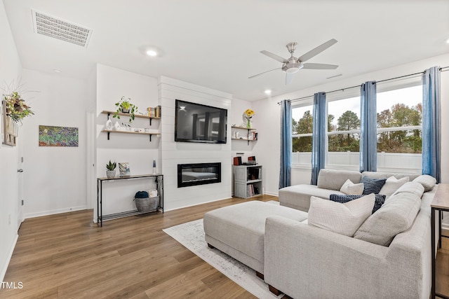 living area featuring a ceiling fan, light wood-style flooring, recessed lighting, a large fireplace, and baseboards