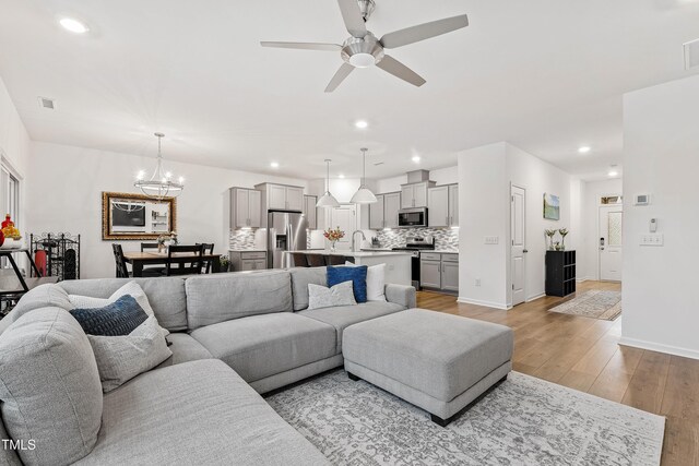 living area with light wood-style floors, a ceiling fan, recessed lighting, a chandelier, and baseboards
