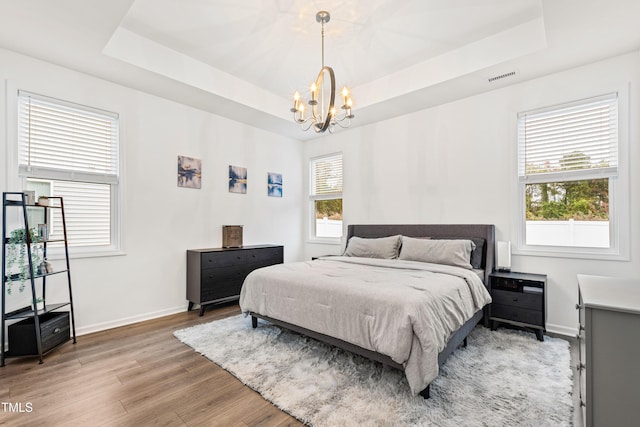 bedroom featuring a tray ceiling, a chandelier, light wood-style flooring, and baseboards