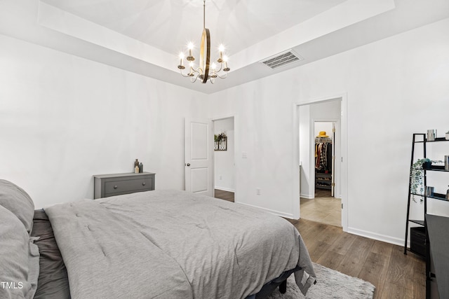 bedroom featuring a tray ceiling, a chandelier, dark wood-style flooring, baseboards, and a walk in closet