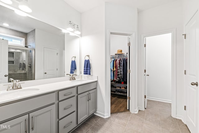 full bath featuring a shower stall, double vanity, a walk in closet, baseboards, and tile patterned flooring