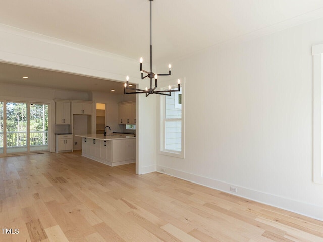 unfurnished living room with crown molding, light hardwood / wood-style floors, a chandelier, and sink