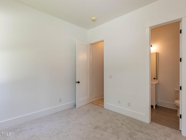 unfurnished bedroom featuring light colored carpet and connected bathroom