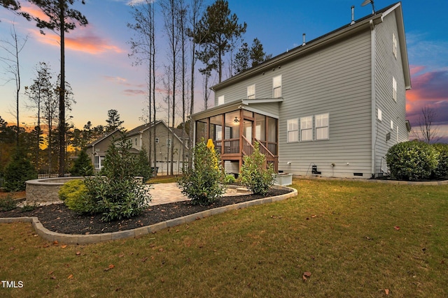 back house at dusk with a yard, a patio, a hot tub, and a sunroom