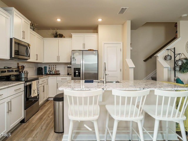 kitchen with white cabinets, decorative backsplash, light wood-type flooring, and appliances with stainless steel finishes