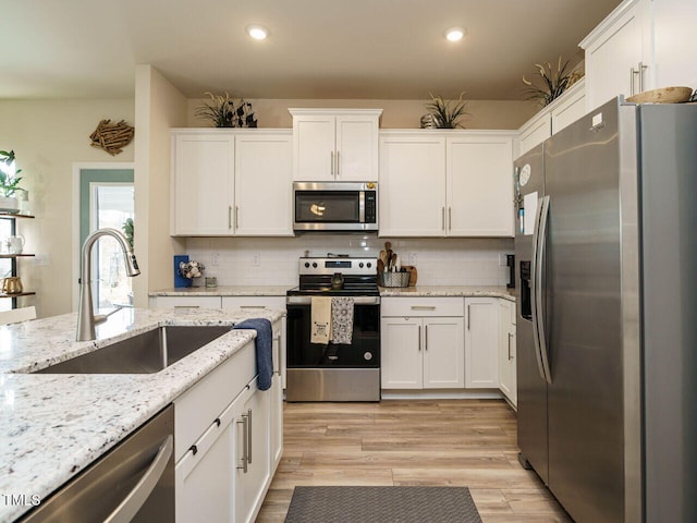 kitchen featuring tasteful backsplash, stainless steel appliances, sink, white cabinets, and light hardwood / wood-style flooring