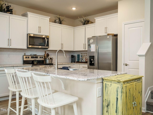 kitchen with stainless steel appliances, a center island with sink, white cabinetry, tasteful backsplash, and wood-type flooring