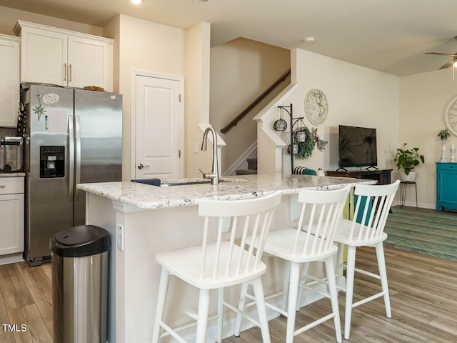 kitchen with white cabinetry, stainless steel refrigerator with ice dispenser, a center island with sink, and light wood-type flooring