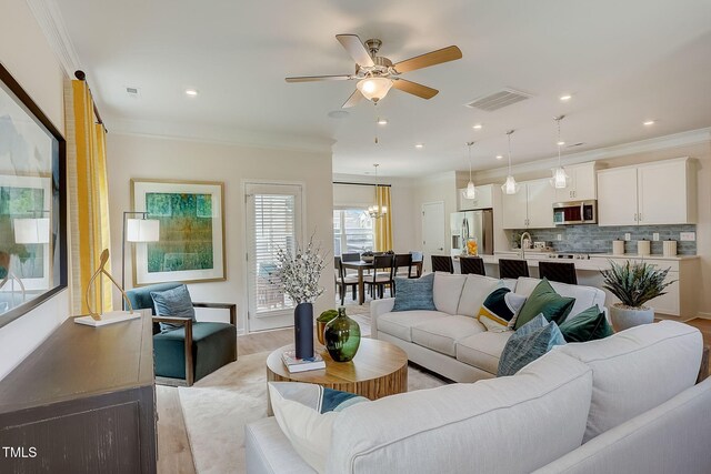 living room with crown molding, sink, light wood-type flooring, and ceiling fan with notable chandelier