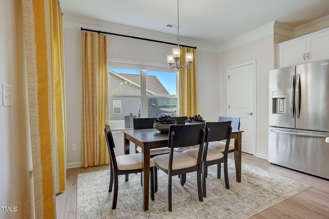 dining space with light hardwood / wood-style floors, ornamental molding, and an inviting chandelier