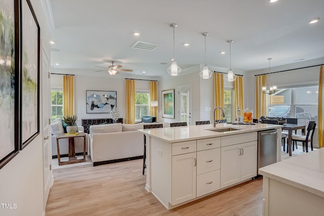 kitchen featuring sink, light wood-type flooring, an island with sink, white cabinetry, and decorative light fixtures