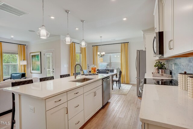 kitchen with decorative backsplash, hanging light fixtures, an island with sink, sink, and stainless steel appliances